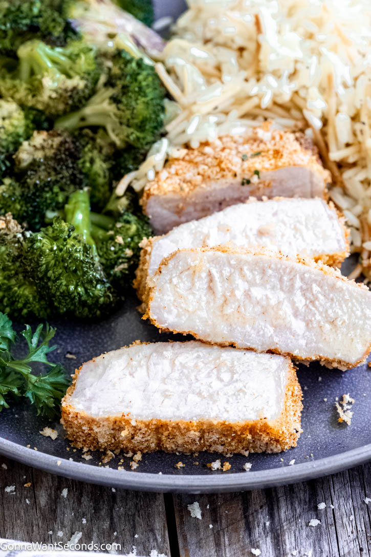 These shake and bake pork chops bake up golden and crisp on the outside while staying tender and juicy inside. #bakedporkchops #porkchops sliced shake and bake pork chops with rice pilaf and roasted broccoli on a plate