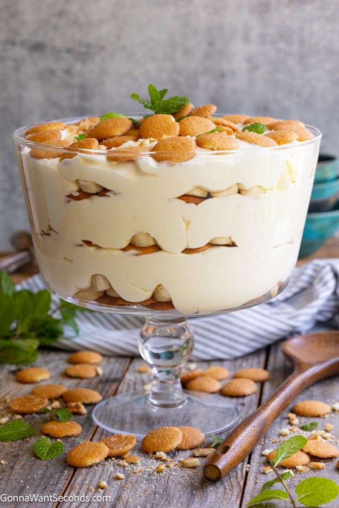 This Magnolia Bakery banana pudding is creamy, light, and perfectly layered with vanilla wafers and bananas. Easy no-bake dessert everyone loves. #bananapudding #nobakedessert Magnolia Bakery banana pudding topped with vanilla wafers and mint leaves in a glass trifle bowl