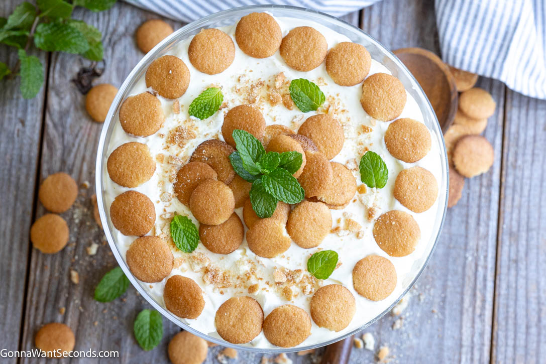 This Magnolia Bakery banana pudding is creamy, light, and perfectly layered with vanilla wafers and bananas. Easy no-bake dessert everyone loves. #bananapudding #nobakedessert Magnolia Bakery banana pudding topped with vanilla wafers and mint leaves in a glass trifle bowl
