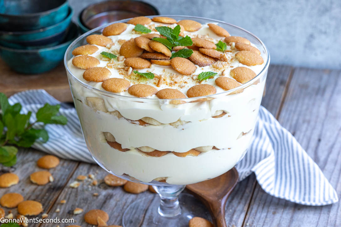 This Magnolia Bakery banana pudding is creamy, light, and perfectly layered with vanilla wafers and bananas. Easy no-bake dessert everyone loves. #bananapudding #nobakedessert Magnolia Bakery banana pudding topped with vanilla wafers and mint leaves in a glass trifle bowl