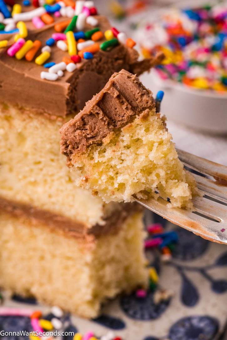 This Yellow Cake with Chocolate Frosting is soft, buttery, and incredibly moist with a fine, bakery-style crumb. #yellowcake #layeredcake fork piercing yellow cake with chocolate frosting