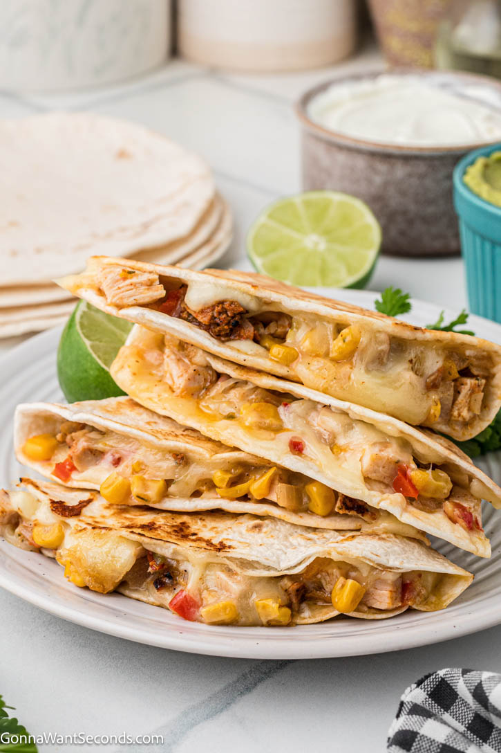 Chicken fajita quesadilla with seasoned chicken, peppers, onions, corn, and melty cheese in a crispy tortilla. Easy, cheesy, and perfect for weeknights. #chickenfajitas #chickenquesadillas slices of Chicken fajita quesadilla on a plate