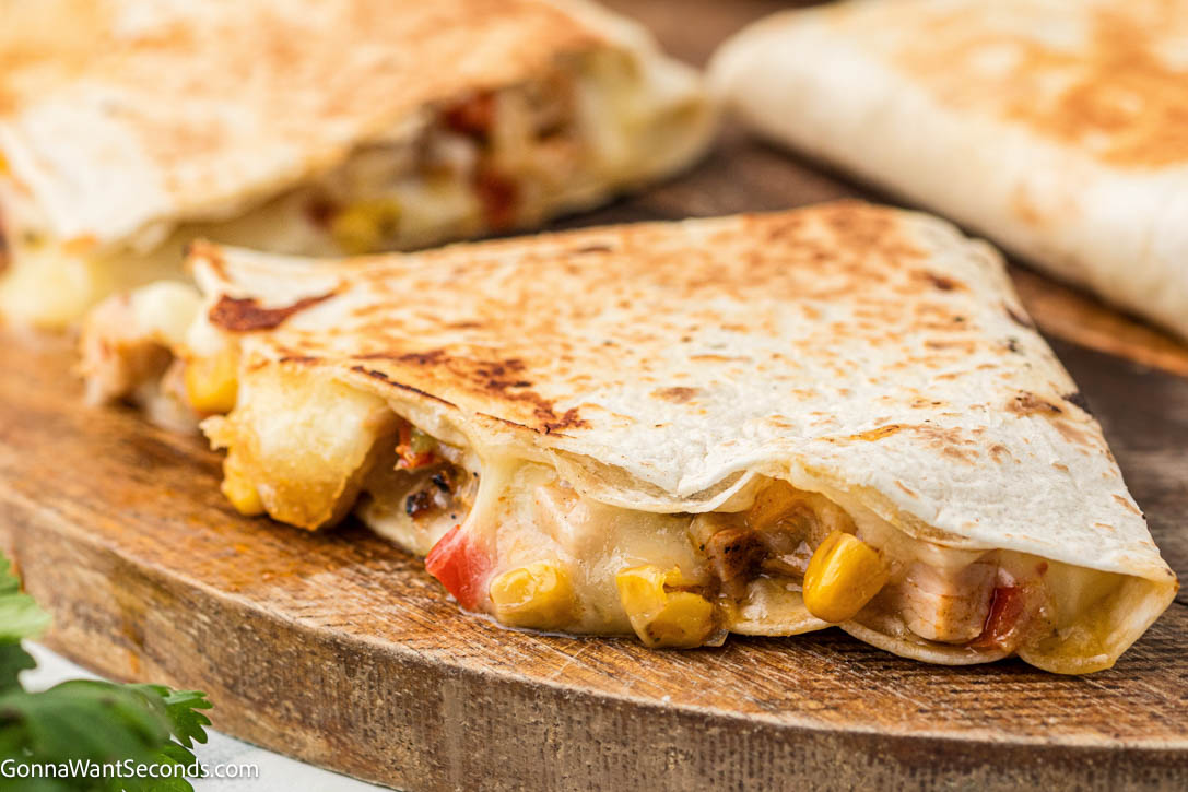 Chicken fajita quesadilla with seasoned chicken, peppers, onions, corn, and melty cheese in a crispy tortilla. Easy, cheesy, and perfect for weeknights. #chickenfajitas #chickenquesadillas a slice of Chicken fajita quesadilla on a wooden board