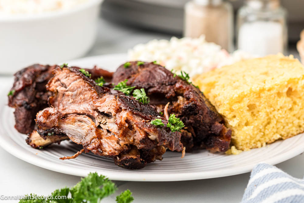 These Crockpot Ribs are tender, juicy, and coated in sticky caramelized BBQ sauce. An easy slow cooker rib recipe everyone loves. #babybackribs #crockpotribs a portion of crockpot ribs with cornbread and rice on the side on a plate