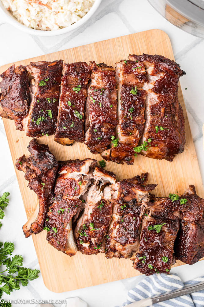 These Crockpot Ribs are tender, juicy, and coated in sticky caramelized BBQ sauce. An easy slow cooker rib recipe everyone loves. #babybackribs #crockpotribs sliced crockpot ribs on a wooden board top shot