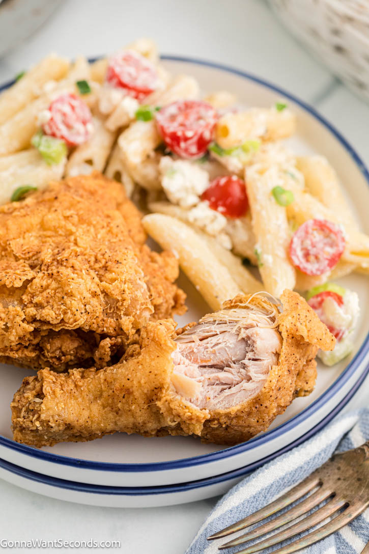Make the best Fried Chicken Recipe with a crispy, golden crust and juicy, tender chicken. This easy buttermilk fried chicken is perfect every time! #friedchicken #buttermilkfriedchicken Two piece Fried Chicken with a bite on it, with pasta salad on the side