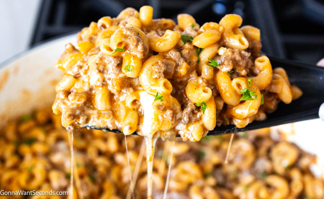 Wooden spatula scooping Hamburger helper with cheese strings drips on the pot