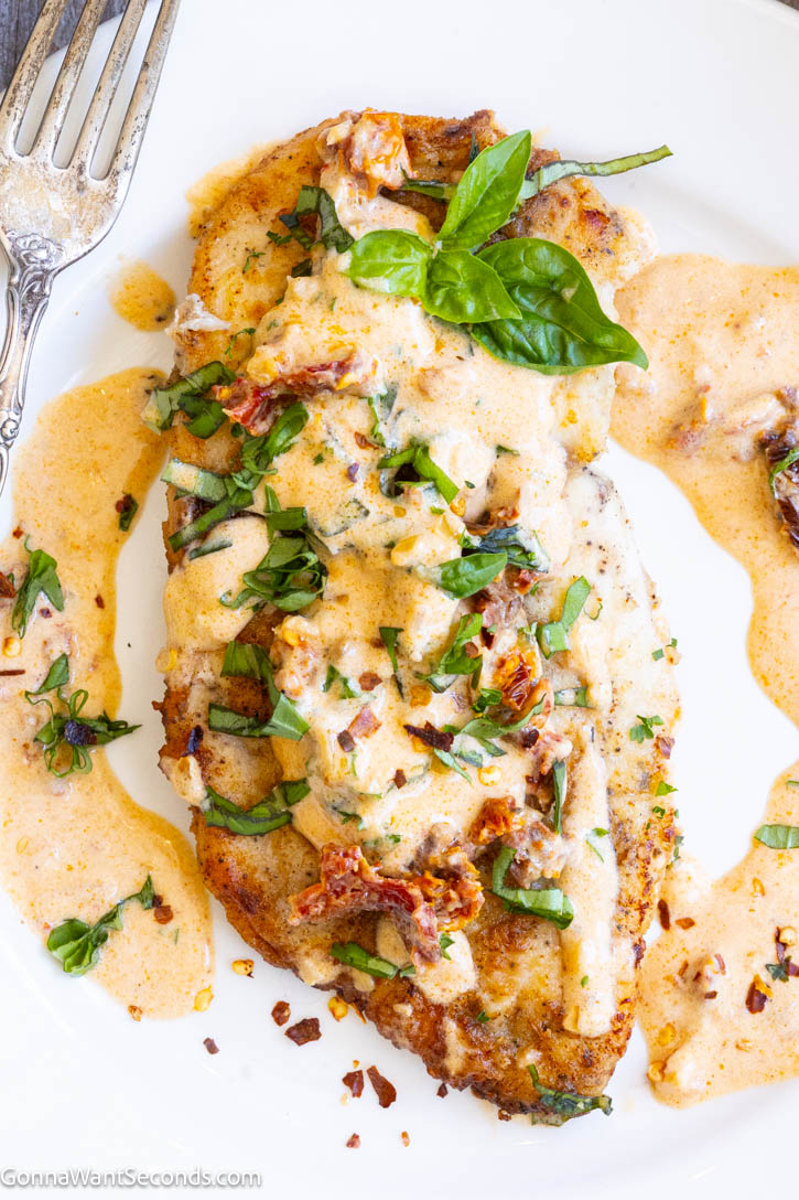 This Marry Me Chicken recipe features juicy chicken breasts in a rich, creamy Parmesan sun-dried tomato sauce. An easy restaurant-quality dinner ready in about 45 minutes. #marrymechicken #easychickenrecipe A piece of Marry Me Chicken smothered in its sauce topped with chopped basil and sun dried tomatoes