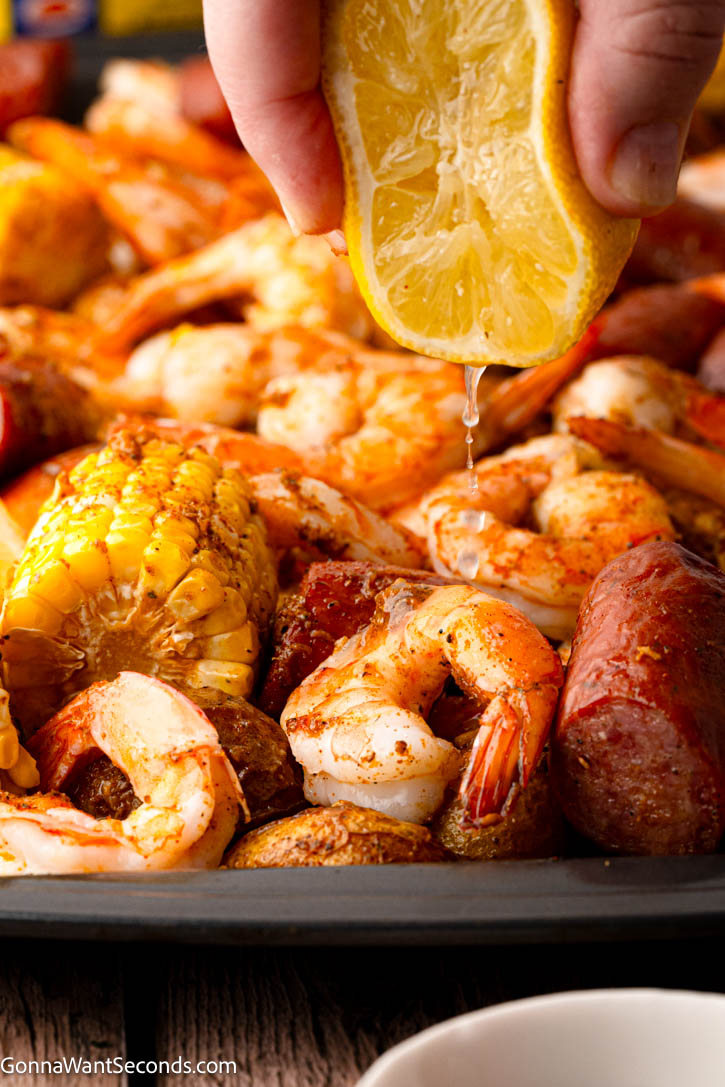 This Sheet Pan Shrimp Boil Recipe is loaded with juicy shrimp, smoky sausage, corn, and potatoes roasted in seasoned garlic butter for an easy one-pan dinner. #shrimpboil #sheetpanrecipes lemon squeezing over Sheet Pan Shrimp Boil