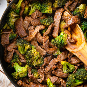 wooden spoon scooping a portion of teriyaki beef and broccoli from a skillet