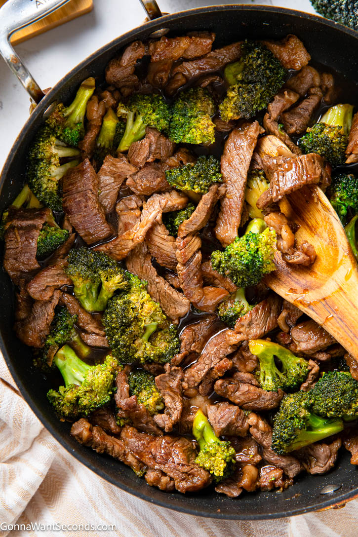 Teriyaki Beef and Broccoli is a quick 35-minute dinner with tender beef, crisp broccoli, and a homemade sweet-savory teriyaki sauce. #teriyaki #beefandbroccoli wooden spoon scooping a portion of teriyaki beef and broccoli from a skillet