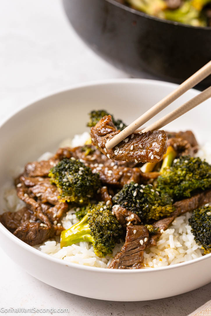 Teriyaki Beef and Broccoli is a quick 35-minute dinner with tender beef, crisp broccoli, and a homemade sweet-savory teriyaki sauce. #teriyaki #beefandbroccoli chopstick picking terkiyaki beef and broccoli from a cup of rice
