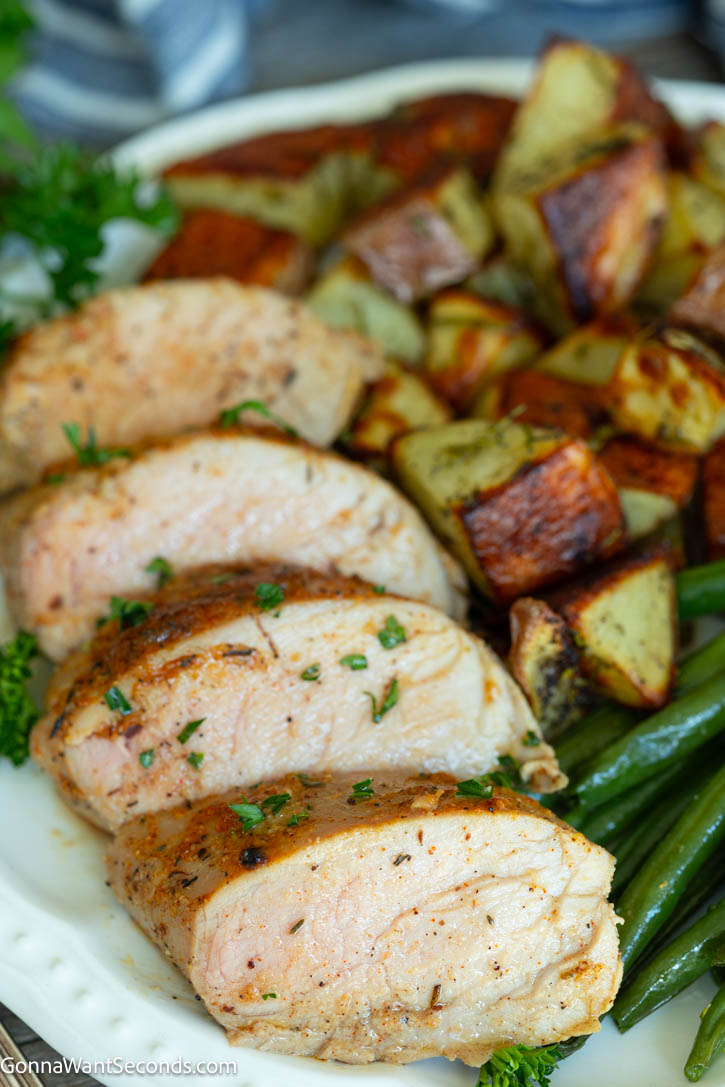 This Baked Pork Tenderloin is juicy, tender, and packed with flavor. An easy oven recipe with no searing or marinating required! #bakedporktenderloin #porktenderloin slices of Baked Pork Tenderloin with roasted veggies on the side, on a plate