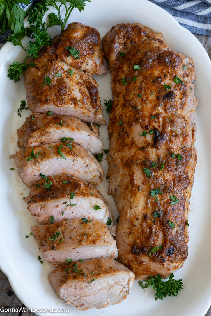 This Baked Pork Tenderloin is juicy, tender, and packed with flavor. An easy oven recipe with no searing or marinating required! #bakedporktenderloin #porktenderloin Sliced and whole baked pork tenderloin, both on a serving platter