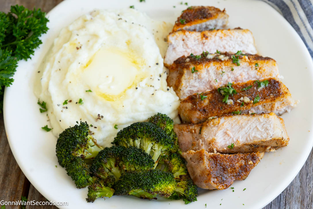 sliced Baked Pork Chops on a plate with mashed potatoes and roasted broccoli on the side