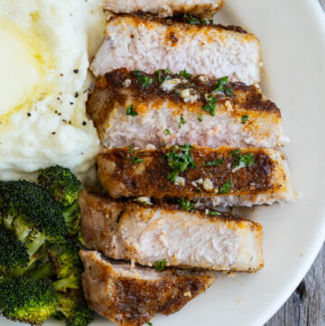 sliced Baked Pork Chops on a plate with mashed potatoes and roasted broccoli on the side