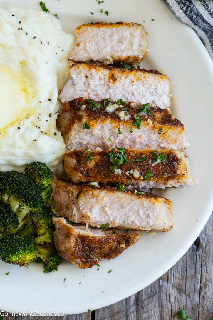These juicy Baked Pork Chops are seasoned with pantry spices, baked to perfection, and finished with rich garlic butter. An easy 30-minute dinner the whole family will love. #bakedporkchops #porkchops sliced Baked Pork Chops on a plate with mashed potatoes and roasted broccoli on the side