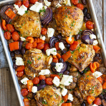 Greek sheet pan chicken with juicy thighs, tender potatoes, colorful vegetables, feta on a sheet pan