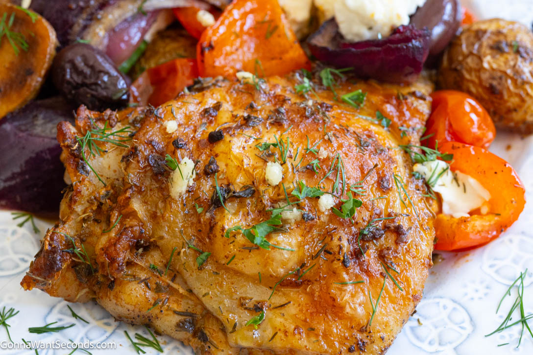 Greek sheet pan chicken with juicy thighs, tender potatoes, colorful vegetables, on a plate