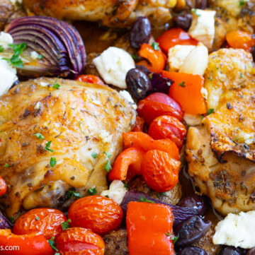 Greek sheet pan chicken with juicy thighs, tender potatoes, colorful vegetables, and feta, close up