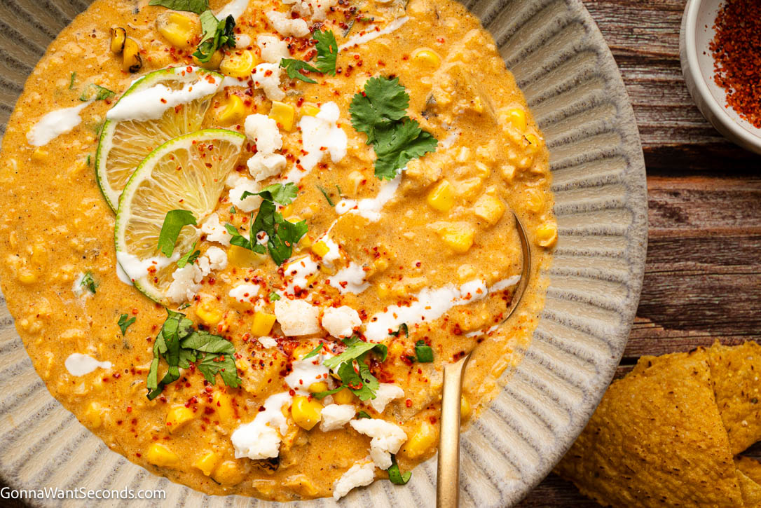 This Mexican Street Corn Soup is rich and creamy with sweet corn, smoky poblano, tender potatoes, lime, cotija, and all your favorite elote flavors. #mexicansoup #streetcornsoup Mexican Street Corn soup topped with lime wedges, cilantro, sour cream and heavy cream in a bowl