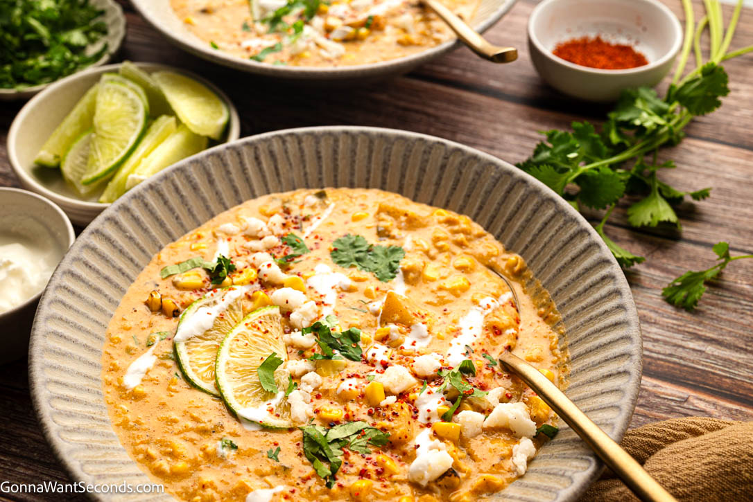 Mexican Street Corn soup topped with lime wedges, cilantro, sour cream and heavy cream in a bowl