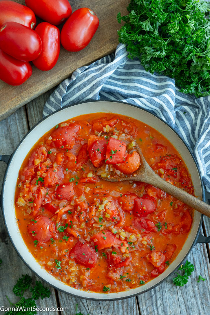 Learn how to make old-fashioned Stewed Tomatoes with fresh Roma tomatoes, onion, celery, butter, and a touch of sugar for a classic comfort-food side. #stewedtomatoes #sidedishes stewed tomatoes in a pan with a wooden spoon