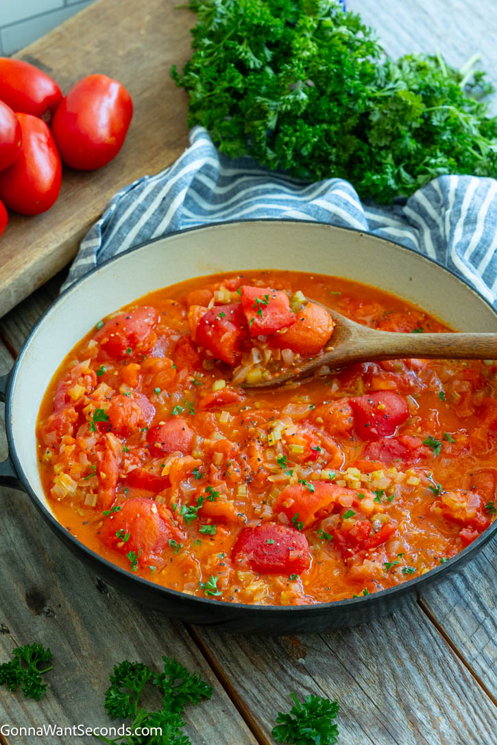 Learn how to make old-fashioned Stewed Tomatoes with fresh Roma tomatoes, onion, celery, butter, and a touch of sugar for a classic comfort-food side. #stewedtomatoes #sidedishes stewed tomatoes in a pan with a wooden spoon