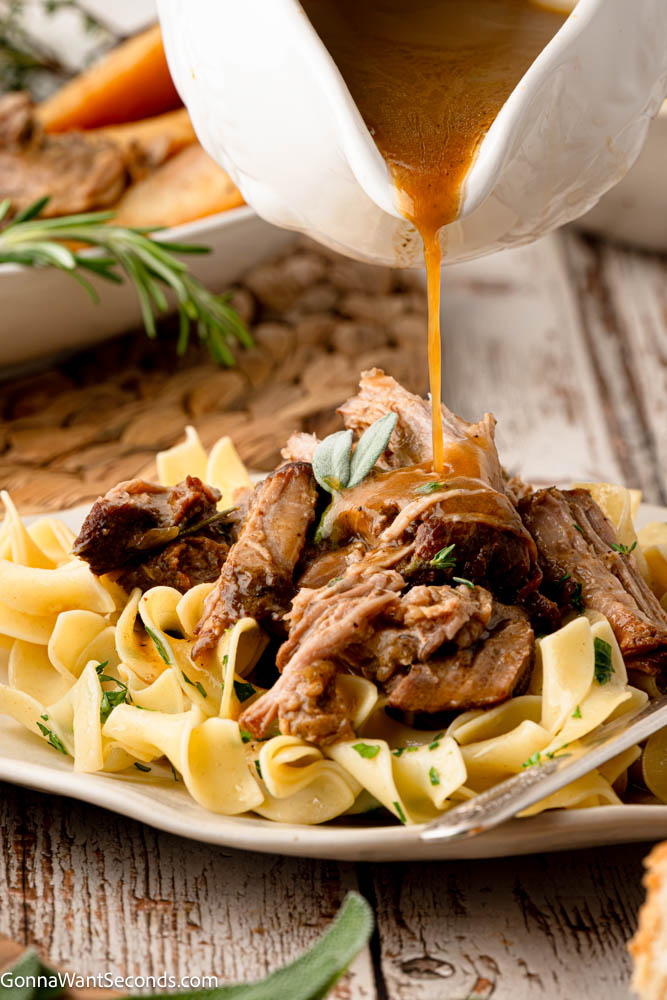 Apple cider braised pork shoulder cooks low and slow until fall-apart tender, with sweet-tart apples, red onions, and a savory cider-Dijon sauce. #braisedporkshoulder #appleciderbraisedpork Gravy pouring over Apple cider braised pork shoulder with pasta
