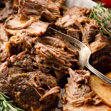 Apple cider braised pork shoulder with apples on a serving platter