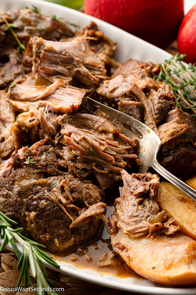 Apple cider braised pork shoulder cooks low and slow until fall-apart tender, with sweet-tart apples, red onions, and a savory cider-Dijon sauce. #braisedporkshoulder #appleciderbraisedpork Apple cider braised pork shoulder with apples on a serving platter