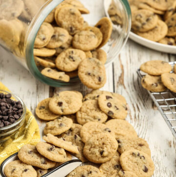 A tipped glass cookie jar spills Mini Chocolate Chip Cookies on the table