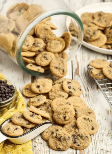 A tipped glass cookie jar spills Mini Chocolate Chip Cookies on the table