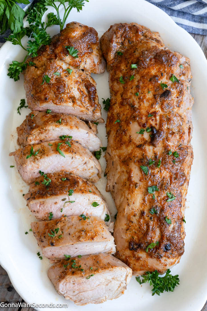 This Baked Pork Tenderloin is juicy, tender, and packed with flavor. An easy oven recipe with no searing or marinating required! #bakedporktenderloin #porktenderloin Sliced and whole baked pork tenderloin, both on a serving platter