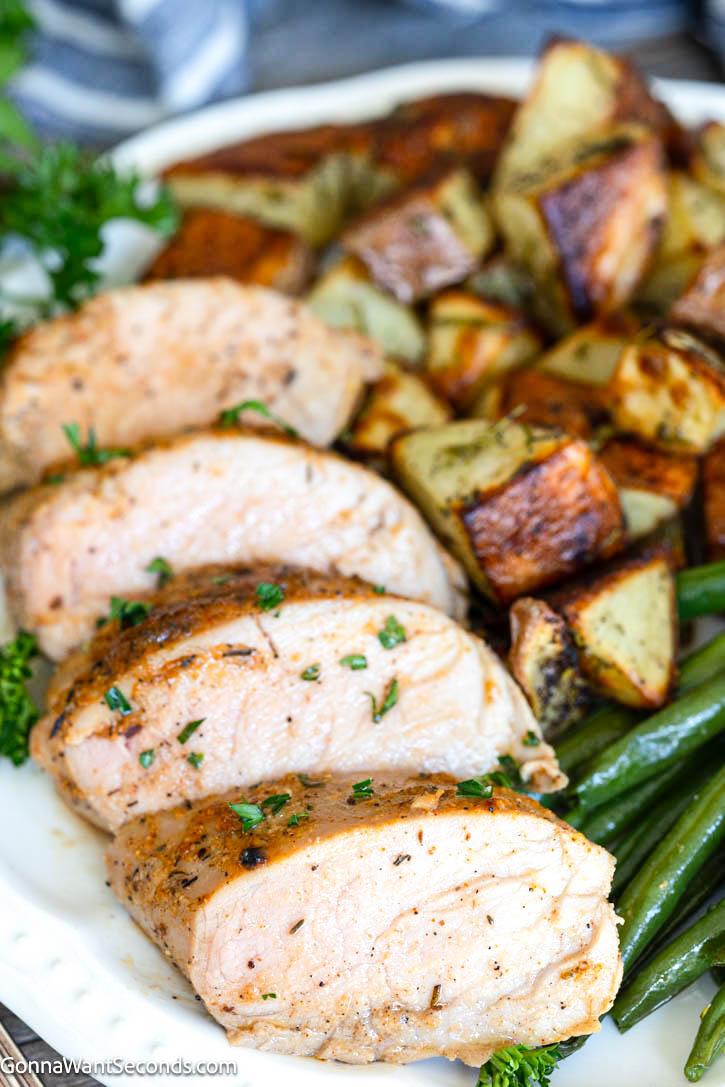 This Baked Pork Tenderloin is juicy, tender, and packed with flavor. An easy oven recipe with no searing or marinating required! #bakedporktenderloin #porktenderloin slices of Baked Pork Tenderloin with roasted veggies on the side, on a plate