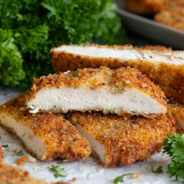 Crispy golden-brown chicken cutlets sliced open on parchment paper, showing juicy white meat inside with fresh parsley garnish