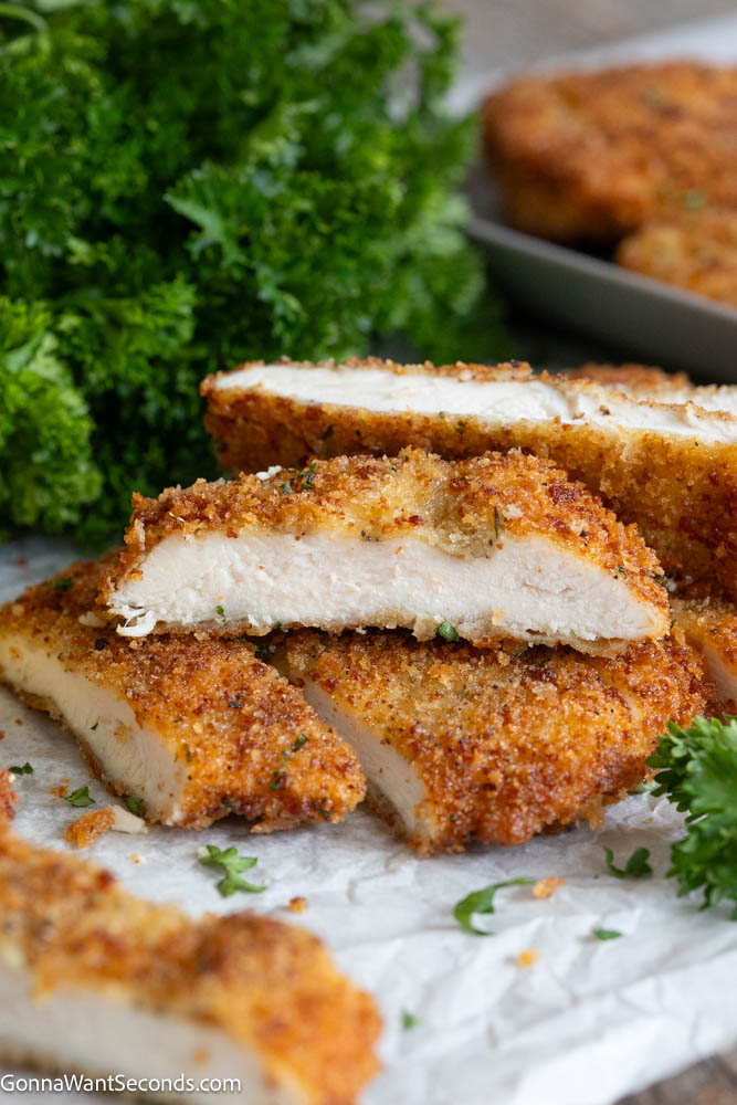 Crispy chicken cutlets with a deeply golden seasoned coating and juicy center. This easy, reliable recipe makes perfect breaded chicken every time! #chickencutlets #friedchickencutlets Crispy golden-brown chicken cutlets sliced open on parchment paper, showing juicy white meat inside with fresh parsley garnish