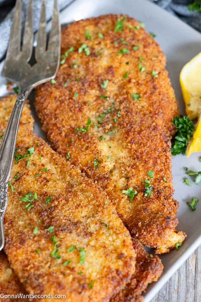 Crispy chicken cutlets with a deeply golden seasoned coating and juicy center. This easy, reliable recipe makes perfect breaded chicken every time! #chickencutlets #friedchickencutlets Golden, perfectly breaded chicken cutlets on a serving platter garnished with fresh chopped parsley and a wedge of lemon