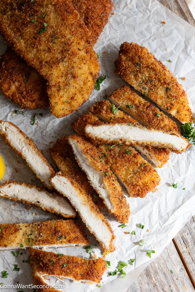 Crispy chicken cutlets with a deeply golden seasoned coating and juicy center. This easy, reliable recipe makes perfect breaded chicken every time! #chickencutlets #friedchickencutlets Crispy golden-brown chicken cutlets sliced open on parchment paper, showing juicy white meat inside with fresh parsley garnish