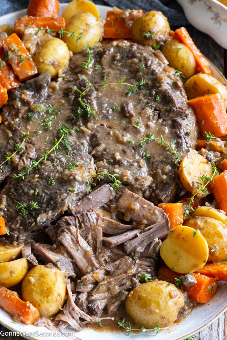 Fall-apart beef, buttery potatoes, and rich gravy—this crockpot pot roast is Sunday dinner at its coziest. A little browning builds big, savory flavor! #potroast #crockpotpotroast Tender Crockpot pot roast served on a platter surrounded by cooked potatoes, sliced carrots, and rich savory gravy sprigged with fresh thyme.