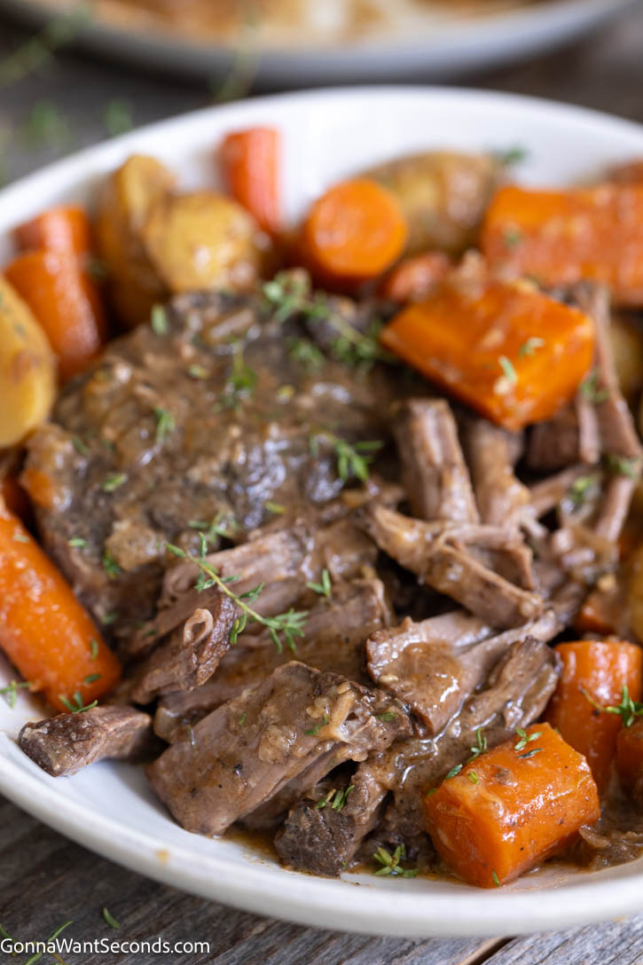 Fall-apart beef, buttery potatoes, and rich gravy—this crockpot pot roast is Sunday dinner at its coziest. A little browning builds big, savory flavor! #potroast #crockpotpotroast Close-up of fork-tender shredded Crockpot pot roast served in a bowl with tender cooked carrot chunks and savory beef gravy