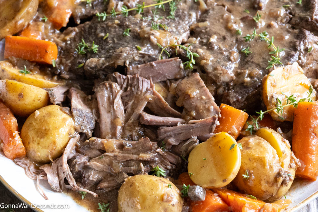 Close-up of fork-tender shredded Crockpot pot roast served in a bowl with tender cooked carrot chunks and savory beef gravy