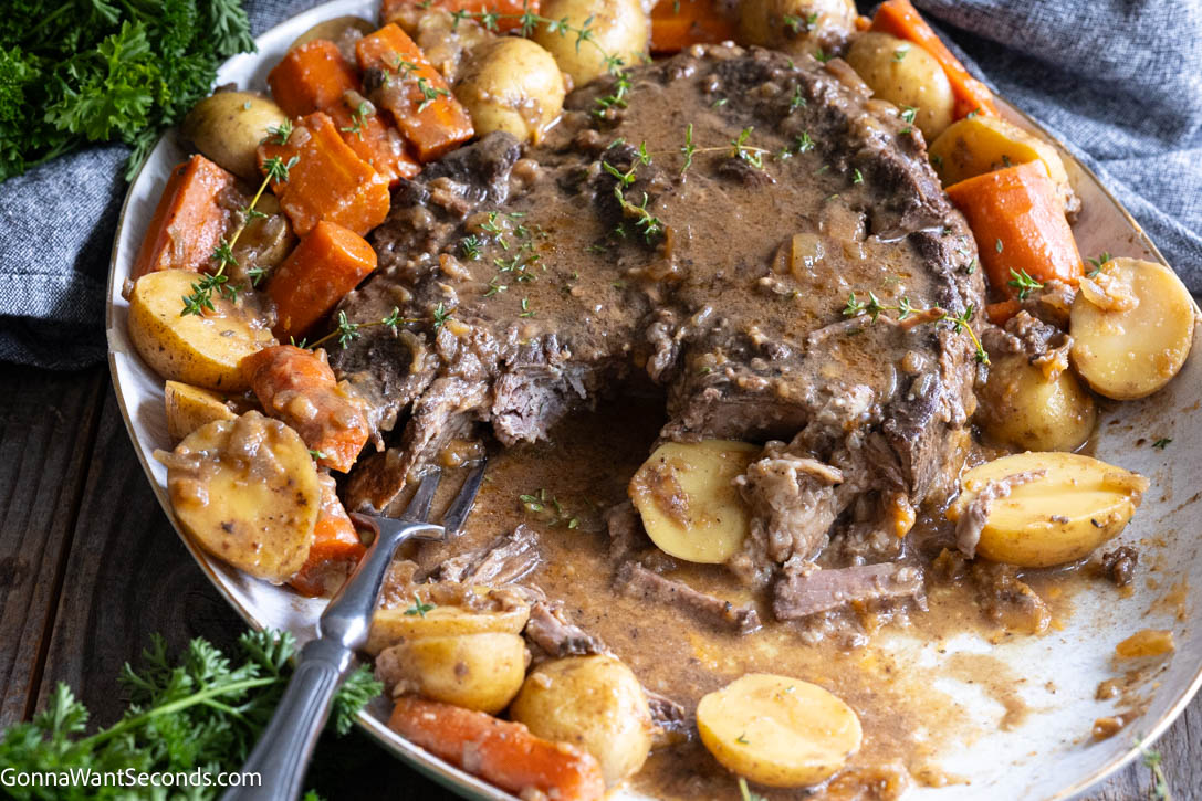 Fall-apart beef, buttery potatoes, and rich gravy—this crockpot pot roast is Sunday dinner at its coziest. A little browning builds big, savory flavor! #potroast #crockpotpotroast A serving platter of Crockpot pot roast with a silver fork pulling apart the juicy beef alongside golden potatoes, carrots, and rich gravy.