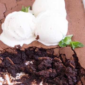 Close-up of scooped Ina Garten brownie pudding showing its rich, gooey chocolate texture, served under scoops of melting vanilla ice cream and mint.